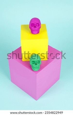 brightly colored plastic skulls on pink and yellow cubes. A cheerful, offbeat composition for Halloween. Minimal color still life photography.