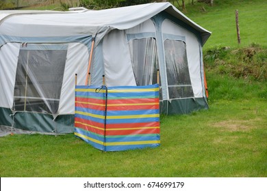 Brightly Colored Windbreak With Dog Lead Hanging From It Giving Privacy And Protection To Caravan And Awning On Rural Camp Site In Wales