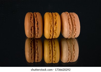Brightly coloured macarons standing vertically on a reflective surface against a black background.