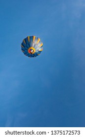 Brightly Coloured Striped Hot Air Balloon Pictured In Blue Skies On The Easter Bank Holiday Flying Above The Cotswolds In Gloucestershire