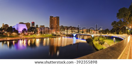 brightly lit Adelaide city CBD with foot bridge across Torrens river. Illumination reflecting in calm waters at sunrise.