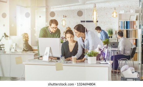 In Brightly Lit And Modern Creative Bureau. In Foreground Three People Discuss Business Issues Using Desktop Computer. In Background Group Of Coworkers Discuss Work Related Matters.