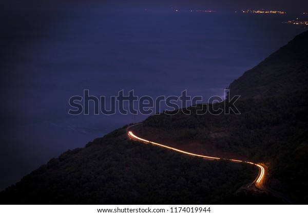 A brightly lit road twisting and curving up\
a mountain in Long Exposure. The winding mountain road with light\
tracks from cars at the\
evening,