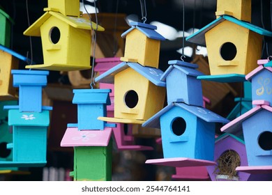 Brightly painted wooden birdhouses of various colors hang in a cheerful display, perfect for adding a touch of nature-inspired decoration to gardens or outdoor spaces. - Powered by Shutterstock