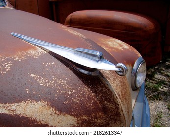 Brightly Shining Chrome Hood Ornament On The Rusty Hood Of A Classic Car.