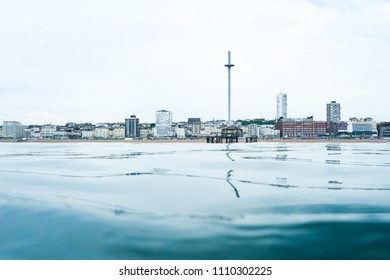 Brighton seafront view point from the sea, at the bottom is a calm glass like flat sea in the middle is the skyline of Brighton, UK, with the I360 viewing tower in the middle and buildings 