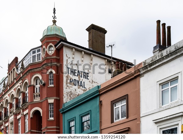 Brighton, Sussex / UK - 31 March 2019: Tired peeling white paintwork with black text announces the19th century Theatre Royal in Brighton. Neighbouring buildings are complementary aqua green and peach.