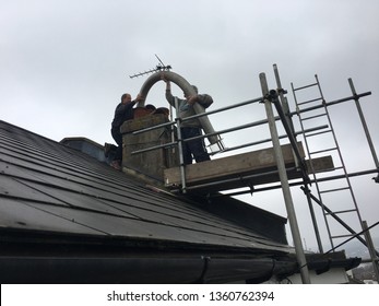 Brighton UK - April 2019 Two Men Repairing  Chimney Lifting Flue Liner Over Chimney Pot On Roof Of A House On Scaffolding 