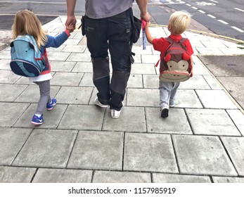 Brighton UK - August 2018 A Dad Walking Two Young Offsprings One On Each Side Holding Their Hands To School Or Back From School Along Tiled Pavement. Back To School