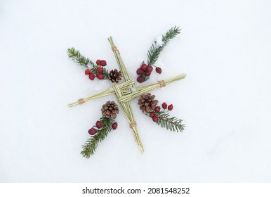 Brigid's cross and fir branches, berries on snow background. symbol of Imbolc sabbat. ireland handmade amulet from straw. Wiccan tradition for blessed, protection. spring-winter pagan ritual. flat lay