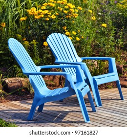 Brilliant blue plastic outdoor Adirondack chairs on the deck in a summer garden.