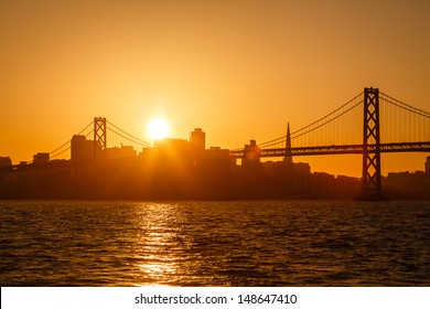 Brilliant golden glow back lights San Francisco skyline and and reflects on the water under the Bay Bridge