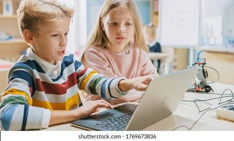 Brilliant Schoolgirl and Schoolboy Talk and Use Laptop to Program Software for Robotics Engineering Class. Elementary School Science Classroom with Children Working on Technology. STEM Education