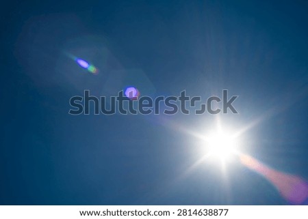 Brilliant sunlight bursts through a cloudless blue sky, creating vivid optical lens flares and radiating long rays of light across the open atmosphere on a hot summer day.