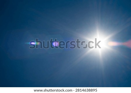 Brilliant sunlight bursts through a cloudless blue sky, creating vivid optical lens flares and radiating long rays of light across the open atmosphere on a hot summer day.