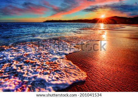 Brilliant vacation destination beach sunrise with colorful sand bright sea foam pink clouds and distant cliffs