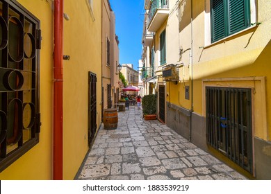 Brindisi, Italy - September 18 2019: A woman walks down a colorful narrow alley towards a cafe in the Italian city of Brindisi Italy, in the Puglia region. - Shutterstock ID 1883539219