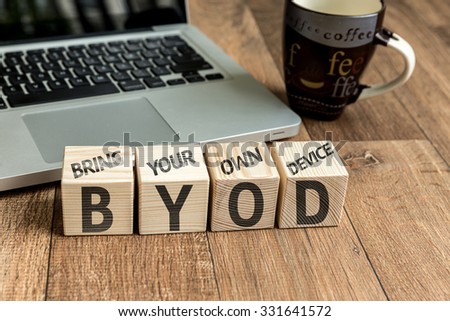 Bring Your Own Device (BYOD) written on a wooden cube in front of a laptop