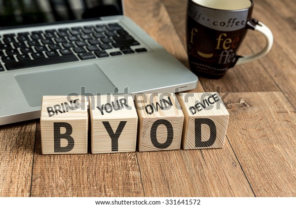 Bring Your Own Device (BYOD) written on a wooden\
cube in front of a laptop