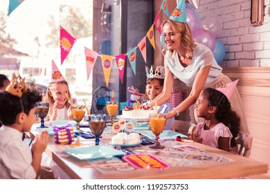 Bringing Cake. Cheerful Loving Mother Smiling And Putting Birthday Cake On The Table For Children