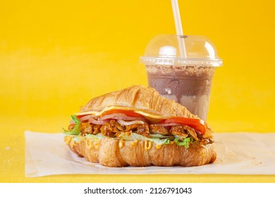 Brioche croissant sandwich with spicy chicken tikka slices tomatoes and cheese with doughnut and cold coffee