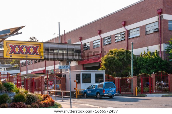 Brisbane, Australia -\
December 8, 2009: Entrance gate to Castlemaine Perkins brewery with\
giant yellow-red XXXX-sign, their beer brand. Silver sky, building\
and car at gate.
