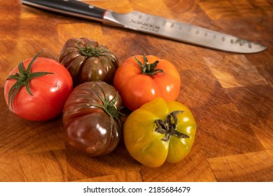 Brisbane, Queensland, Australia - October 15th 2021: fresh bunch raw tomatoes in different colours on a wooden chopping board and knife in the background ready to be cut. healthy options for lunch 