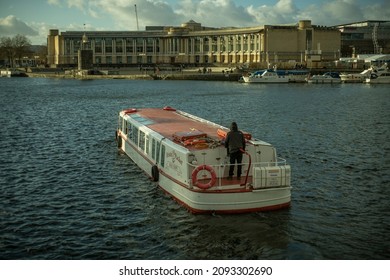 Bristol, England, UK - 12.05.2021: A man sails his boat through Millenium Square on the River Avon. Lloyds Commercial Finance in the background.