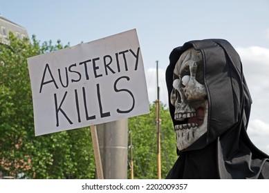 BRISTOL, UK - JULY 8, 2015: A Masked Anti-austerity Demonstrator Holds A Placard With The Slogan “AUSTERITY KILLS”.