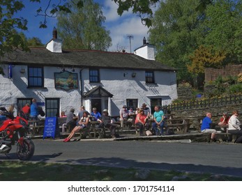 Britannia Inn, Elterwater, Cumbria, UK - May 7 2017: People Outside A Traditional Rural Pub Enjoying The Sunny Weather In The English Lake District With A Bright Red Motorbike In The Foreground