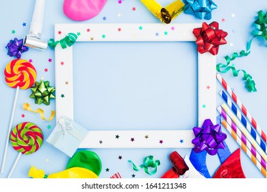 Brithday background with white wooden frame and colorful festive accessories. Copy space. Flat lay. Bows, lollipops, baloons, straws, streamers for holidaay concept