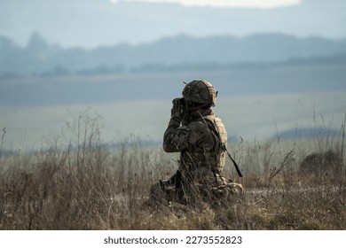 British army infantry soldier using binoculars to scan distance for enemy threats, military exercise, Wiltshire UK