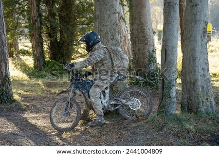 British army Paratrooper riding a Qiulong Surron Sur-Ron Firefly electric motorcycle along a muddy track on a military exercise