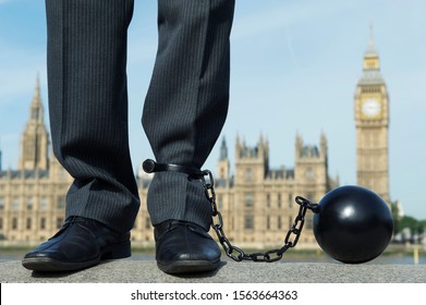 British Businessman With Ball And Chain Shackled To His Ankle Standing In Front Of The Houses Of Parliament At Westminster, London, UK