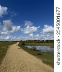 British Countryside landscape with blue sky, beautiful cloud patterns, gravel path, a pond and rolling hills. It’s a national park. There is a reflection of the clouds in the water.