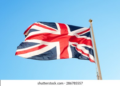 British Flag Or Union Jack Flying On A Flag Pole Against A Blue Sky