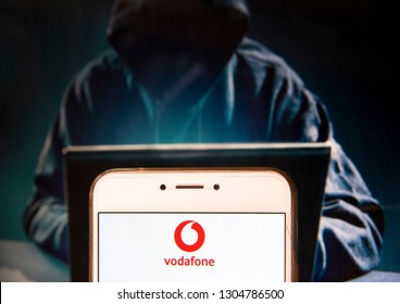 British multinational telecommunications corporation and phone operator Vodafone logo is seen on an Android mobile device with a figure of hacker in the background.