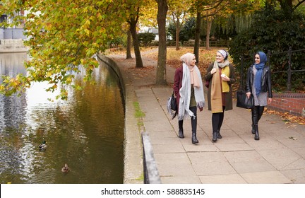 British Muslim Female Friends Walking By River In City