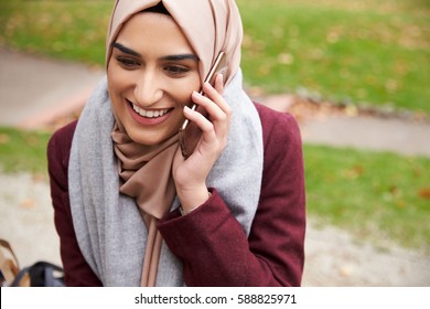 British Muslim Woman On Break Using Mobile Phone In Park - Powered by Shutterstock