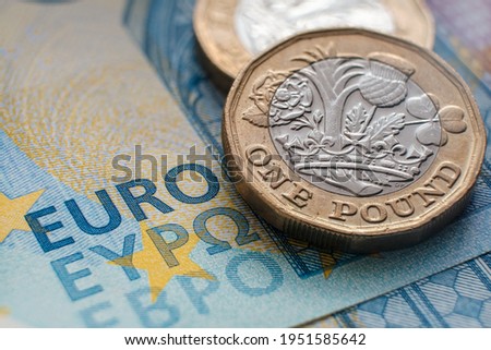 British one pound coin placed on top of 20 EURO banknote with visible words 