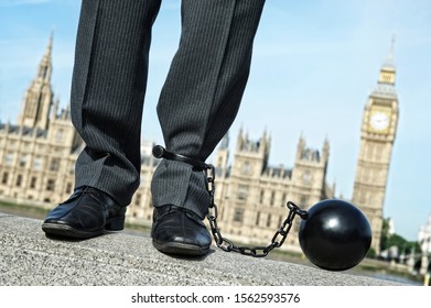 British Politician With Ball And Chain Shackled To His Ankle Standing In Front Of The Houses Of Parliament At Westminster, London, UK