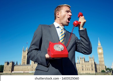 British politician yelling into an old red rotary telephone hotline in front of the Houses of Parliament at Westminster, London, UK