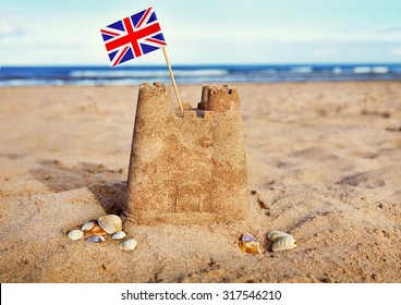 British Seaside Traditional Sand Castle On The Beach With Union Jack Flag And Shells