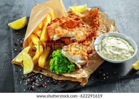 British Traditional Fish and chips with mashed peas, tartar sauce on crumpled paper.