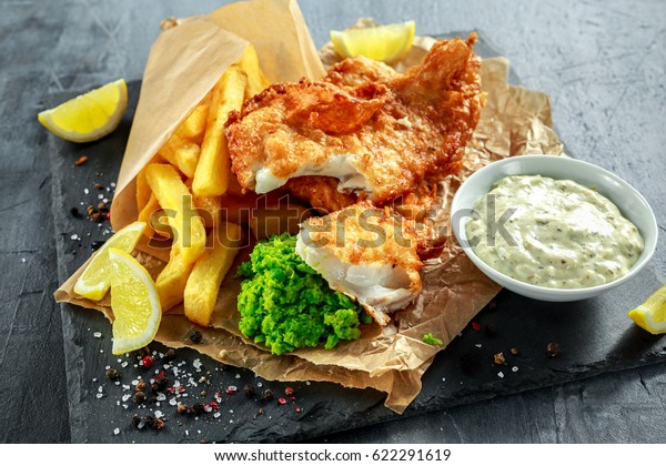 British Traditional Fish and chips with\
mashed peas, tartar sauce on crumpled\
paper.