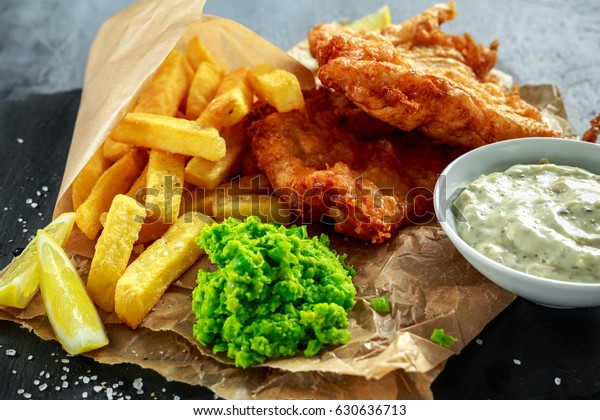 British Traditional Fish and chips with
mashed peas, tartar sauce on crumpled
paper.