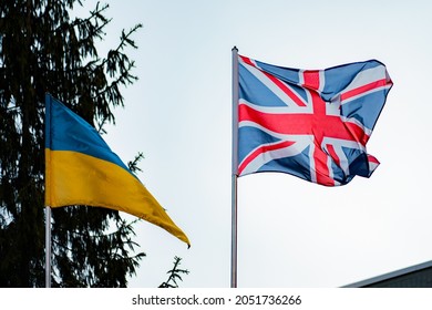 British and Ukrainian flags against the background of blue sky and spruce. Nature. Relationship. Diplomacy. Politics. Friendship. UK. Ukraine. Business. Agreement