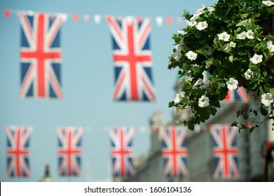 British Union Jack Flags Flying In The Summer Sky Behind A Flowering Planter On A Sunny London Street