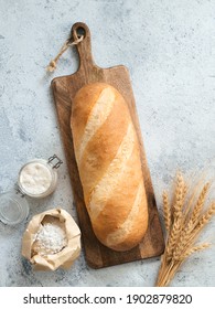 British White Bloomer or European sourdough Baton loaf bread on gray cement background. Fresh loaf bread, glass jar with sourdough starter, flour in paper bag and ears. Top view. Copy space. Vertical