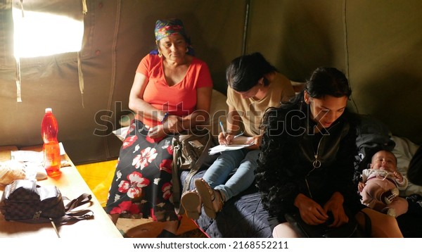 BRNO, CZECH REPUBLIC, JUNE 10, 2022: Refugees\
Ukraine Gypsy fill in documents for visas and social financial\
benefits in tent immigrants detention camp Gypsies people family\
Roma children